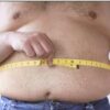 Person measuring waist with yellow tape measure.