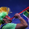 Person blowing vuvuzela with colorful headdress.