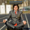 Businessman balancing briefcase while meditating outdoors.
