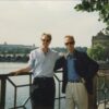 Two men posing by a riverside railing.