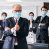 Business team wearing masks, giving thumbs up.