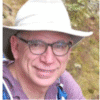 Man wearing hat and glasses, smiling outdoors.